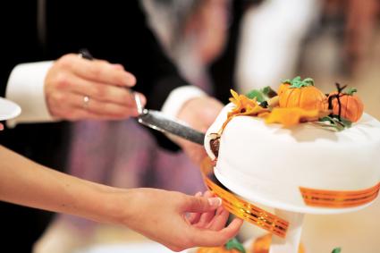 Les mariés ont découpé un beau gâteau blanc de mariage décoré de citrouilles orange