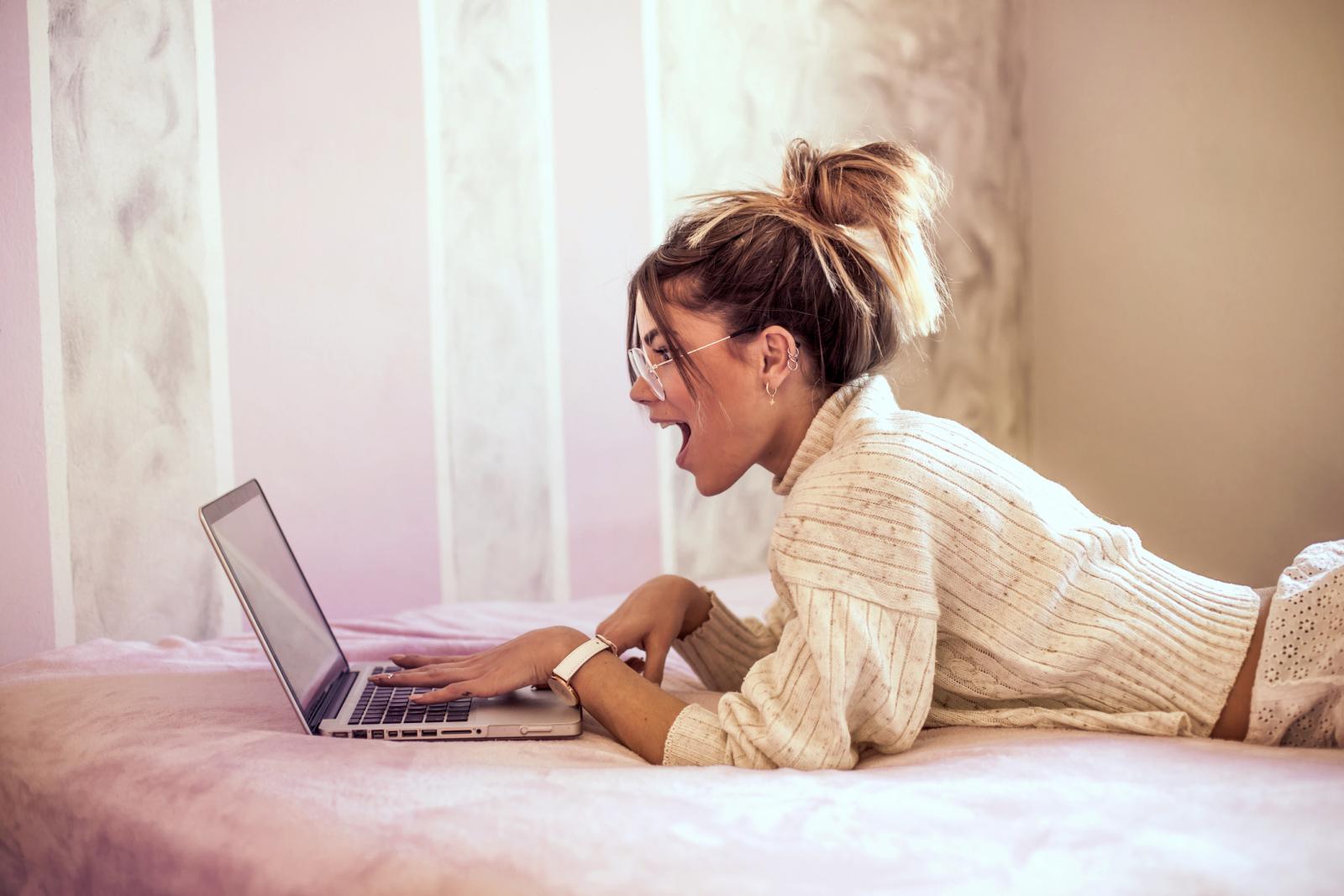 Surpris jeune femme allongée sur le lit à l'aide d'un ordinateur portable 