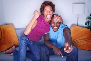 African couple cheering on sofa