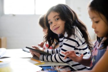 Portrait of smiling girl using digital tablet in classroom