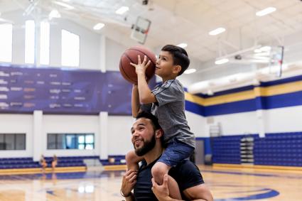 Le père a un fils sur les épaules pour tirer des paniers au gymnase