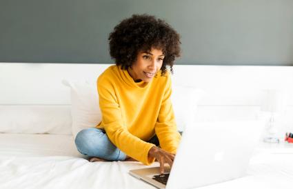 femme assise sur le lit en utilisant un ordinateur portable