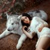Girl with dark hair is lying on gray-white forest wolf